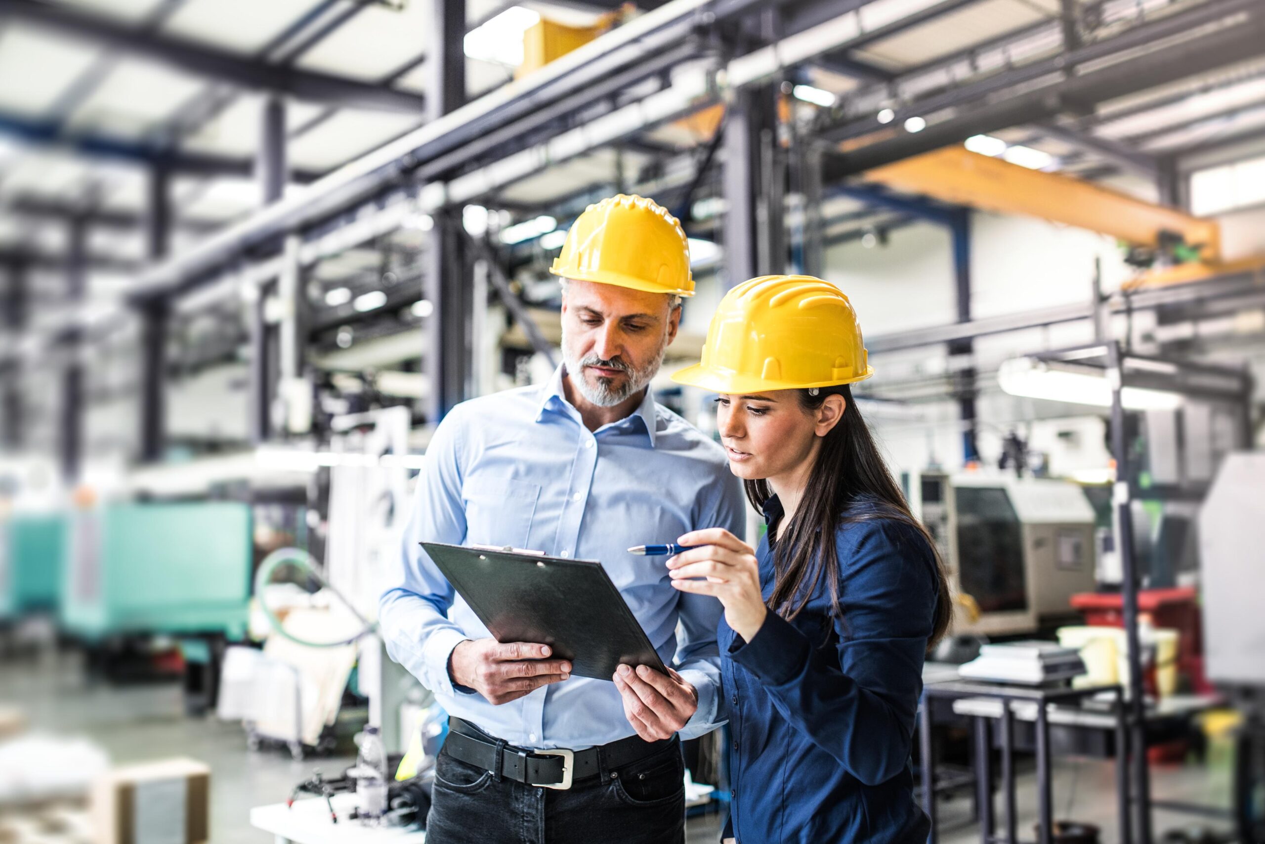 Two project managers standing in modern industrial factory. Manufacturing facility with robotics, robotic arms and automation.