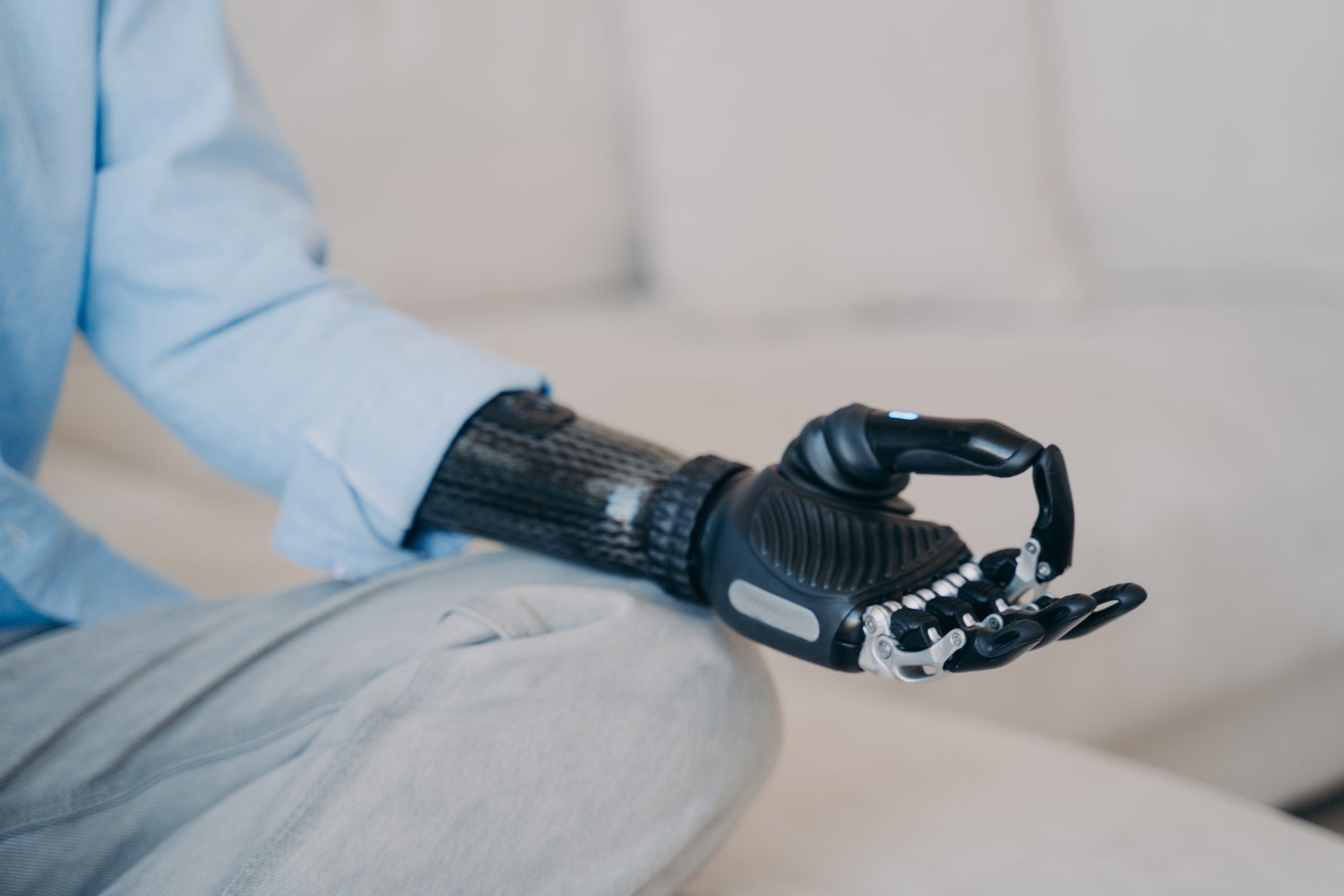 Cyber hand of disabled person which is sitting in lotus pose on couch. Robotic arm in meditation.